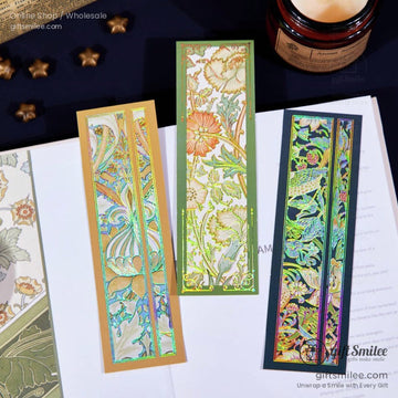 A set of three holographic bookmarks featuring intricate floral Art Nouveau designs, placed on an open book
