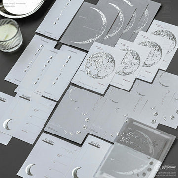A collection of moon phase-themed silver foil stationery cards displayed neatly on a dark surface