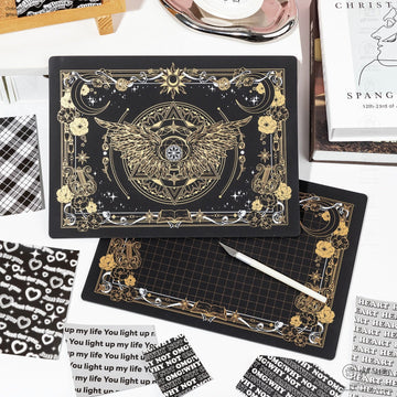 Black and gold celestial-themed cutting mat with intricate wing and moon design.