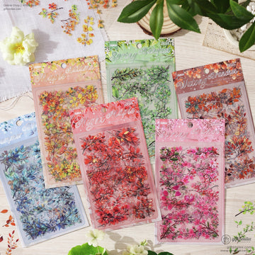 A set of six seasonal floral sticker packs displayed on a wooden surface with delicate flowers and leaves surrounding them