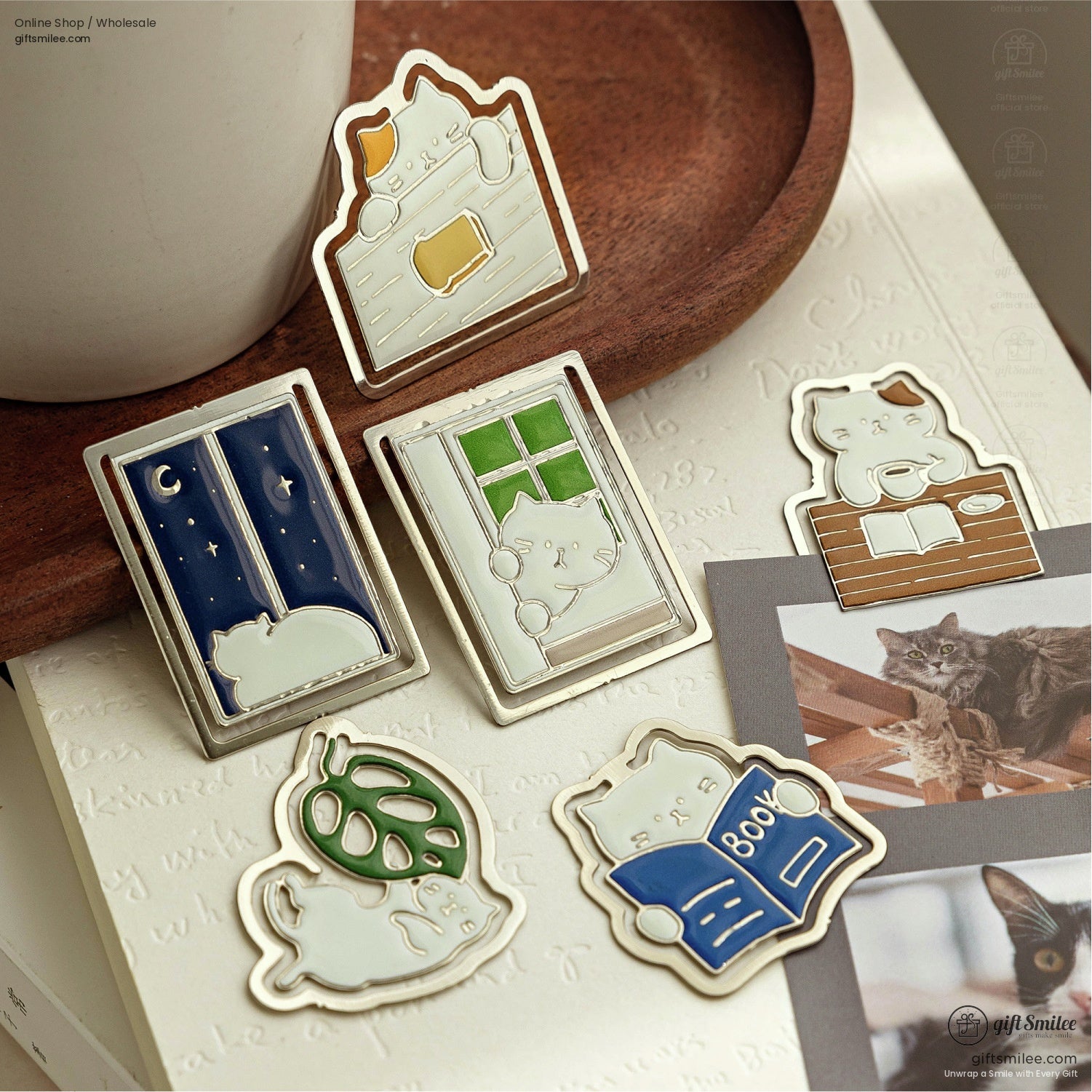 A set of six cat-themed enamel bookmarks displayed on a wooden tray and book.