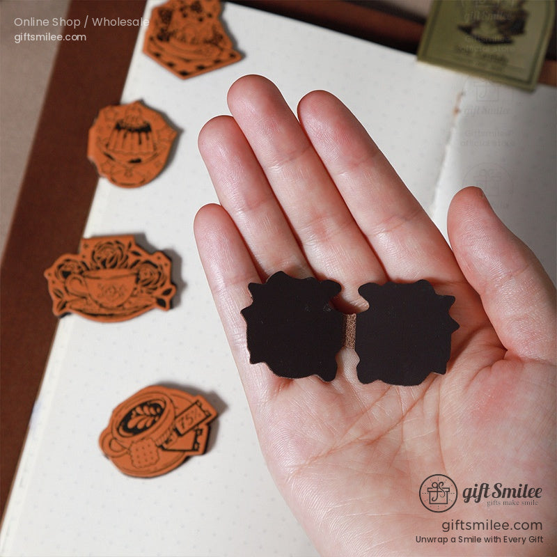 Hand holding two magnetic leather bookmarks with intricate designs.