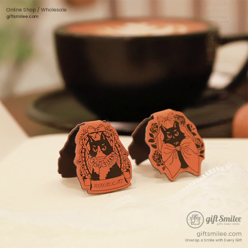 Close-up of cat-themed leather bookmarks styled near a cup of hot chocolate.