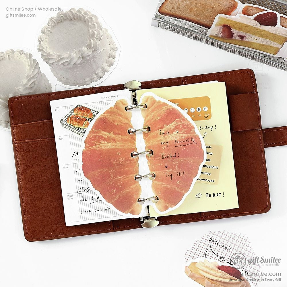 A journal decorated with bread-shaped note paper stickers and text annotations, surrounded by pastry stickers
