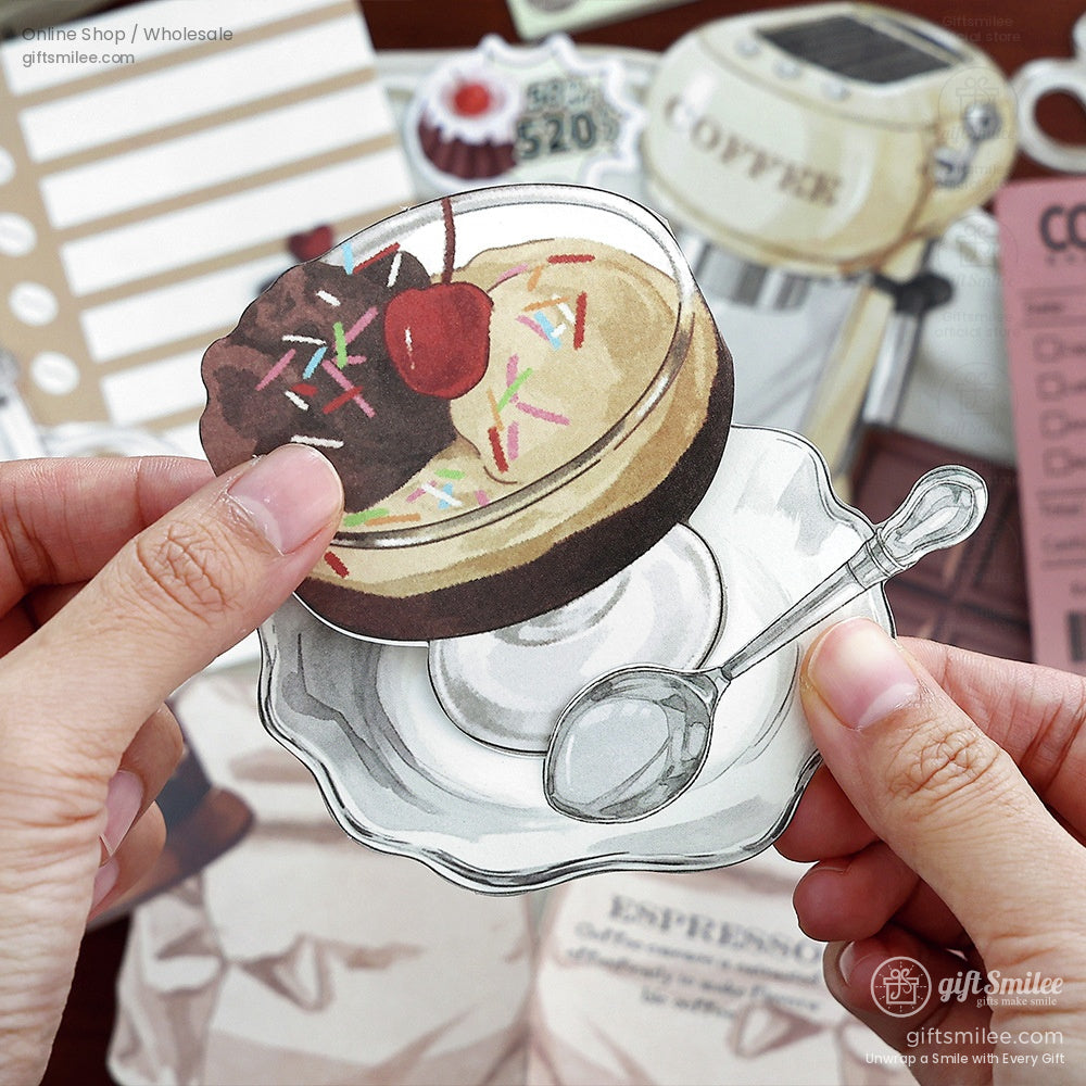 Close-up of a hand holding a vintage-style dessert sticker featuring a chocolate sundae with a cherry on top