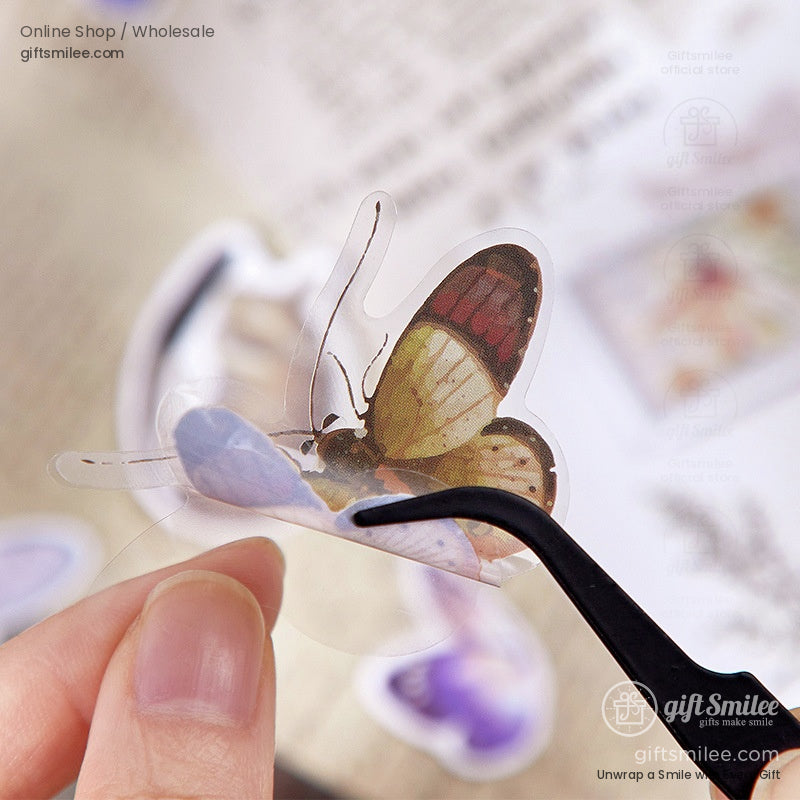 A close-up of a butterfly-themed transparent sticker being delicately handled with tweezers