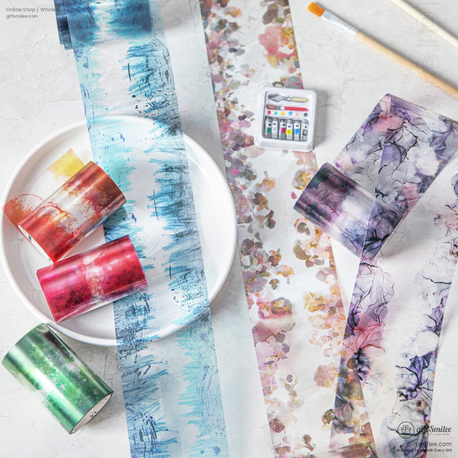 A collection of watercolor washi tape rolls with abstract and floral patterns, displayed with art supplies.
