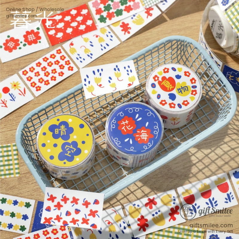 Three washi tape rolls with vibrant flower-themed designs in a wire basket surrounded by decorative stickers