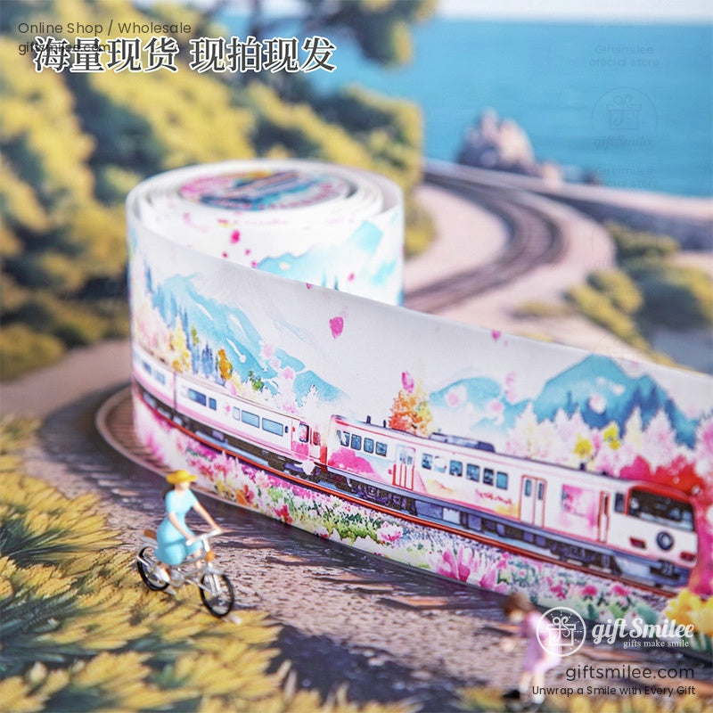 Close-up of a washi tape roll with a train design, surrounded by a picturesque countryside scenery