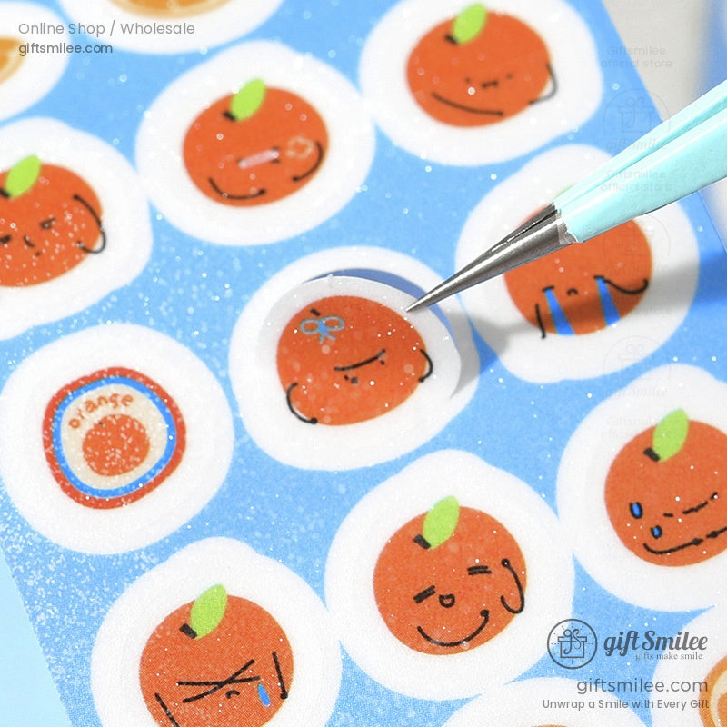 Close-up of orange fruit stickers with unique faces on a blue washi tape roll