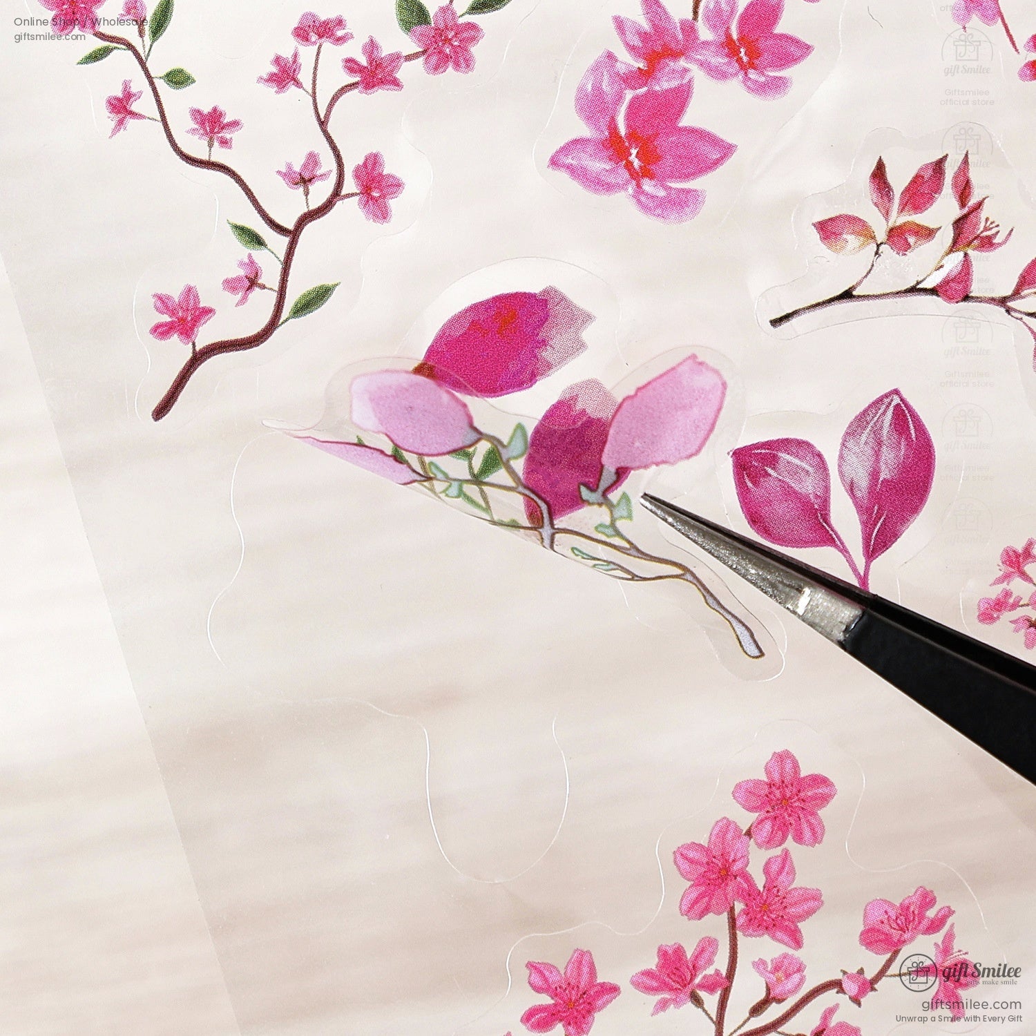 A pair of tweezers lifting a pink floral sticker, highlighting its fine details and vibrant colors