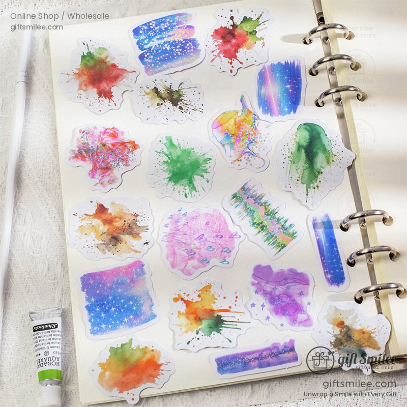Assorted watercolor splash stickers on a ring binder journal in a creative workspace