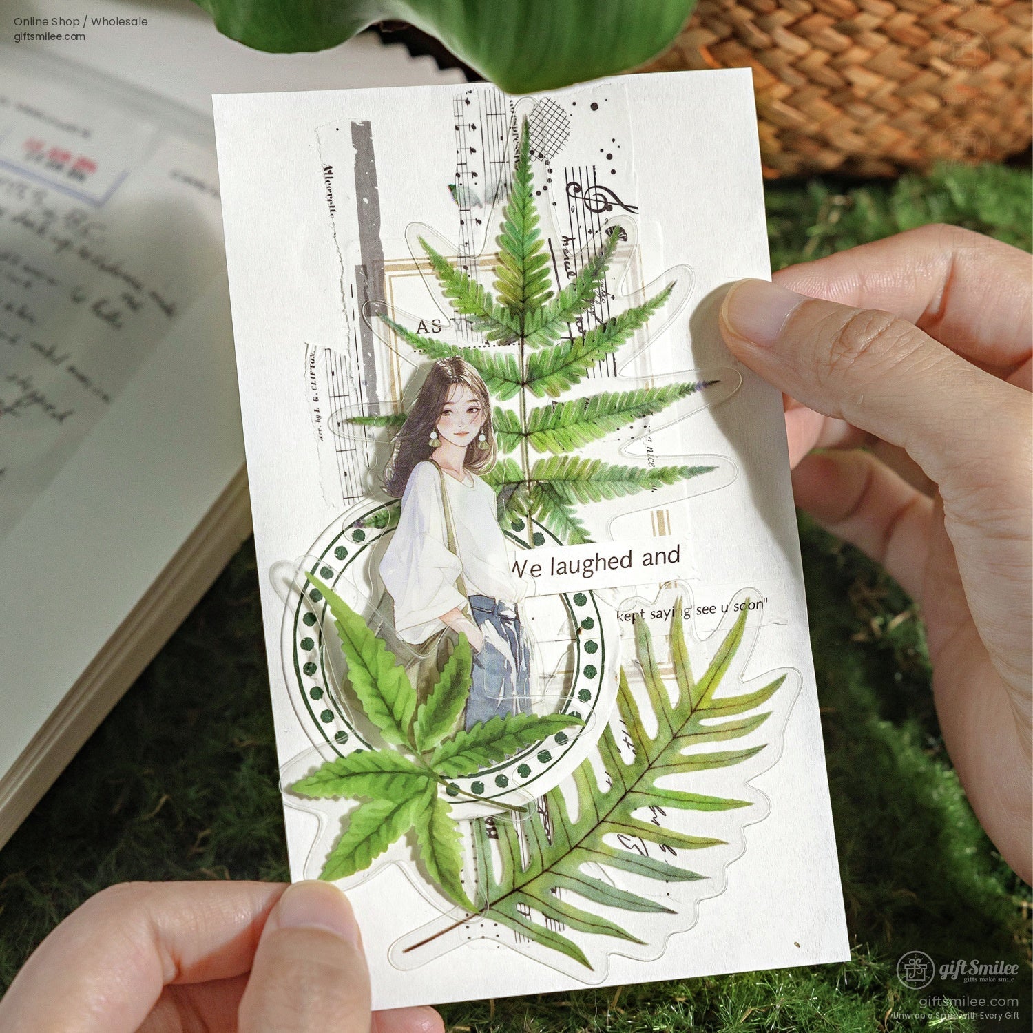 Person holding a nature-themed sticker with fern designs over a scrapbook page