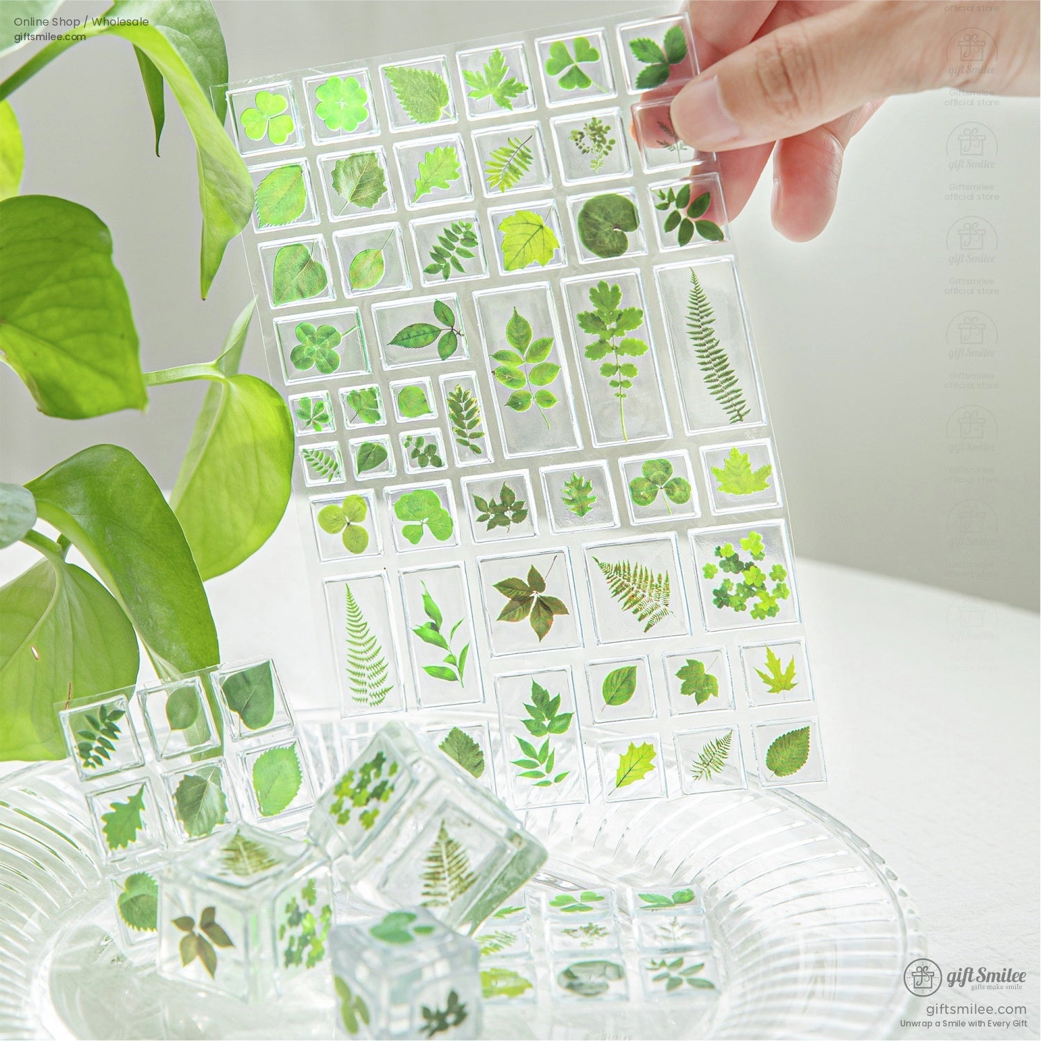 Green leaf-themed transparent sticker sheet being held above a glass plate surrounded by greenery