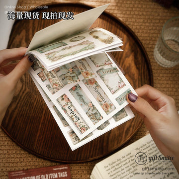 Close-up of hands flipping through a booklet of vintage-inspired scrapbook stickers with floral and antique designs