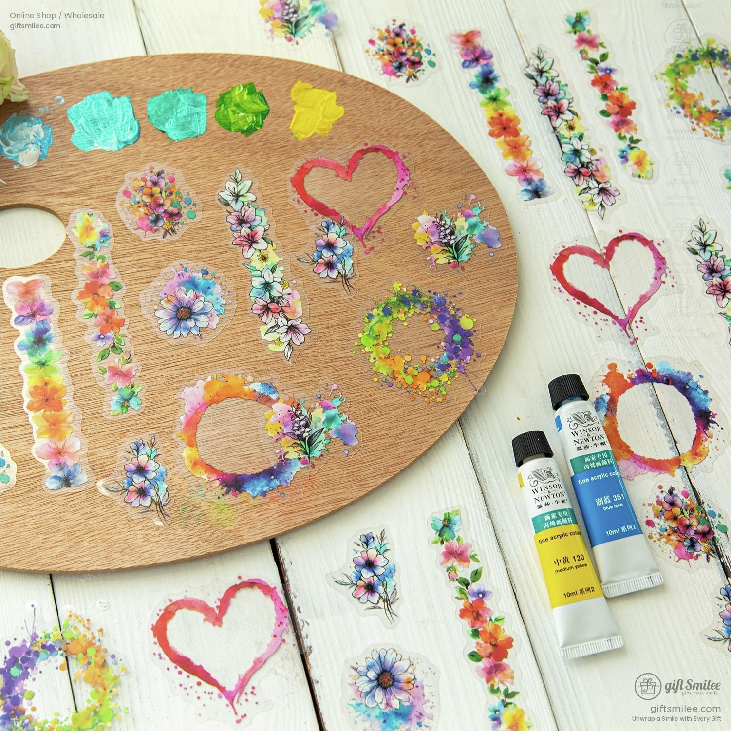 Wooden palette adorned with floral watercolor stickers in various shapes near paint tubes
