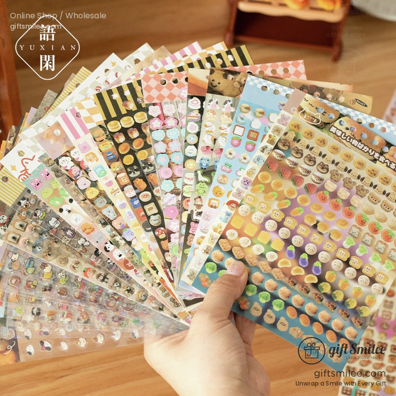 A hand holding a fan of colorful, kawaii-themed sticker sheets featuring adorable characters, food icons, and patterns
