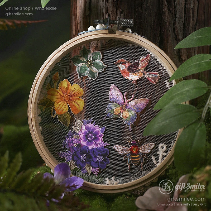 A set of embroidery stickers featuring flowers, butterflies, birds, and a honeybee displayed in a wooden hoop with a forest backdrop