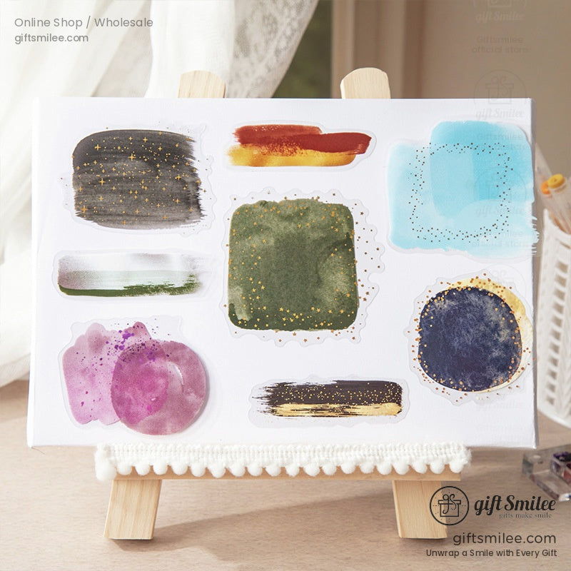 A set of abstract watercolor stickers with galaxy-inspired designs on a mini easel